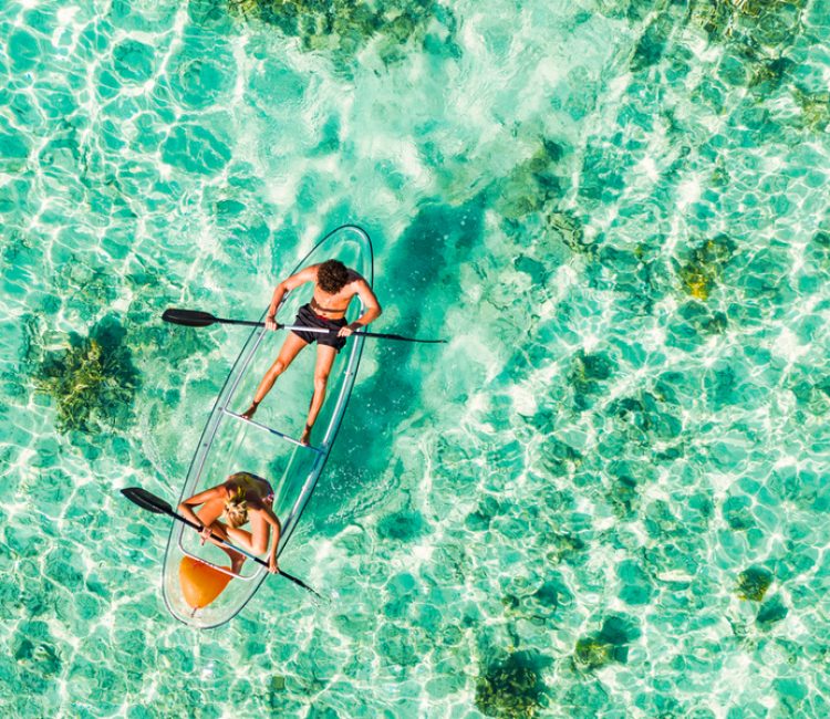Young couple paddling on glass bottom kayak in tropical ocean