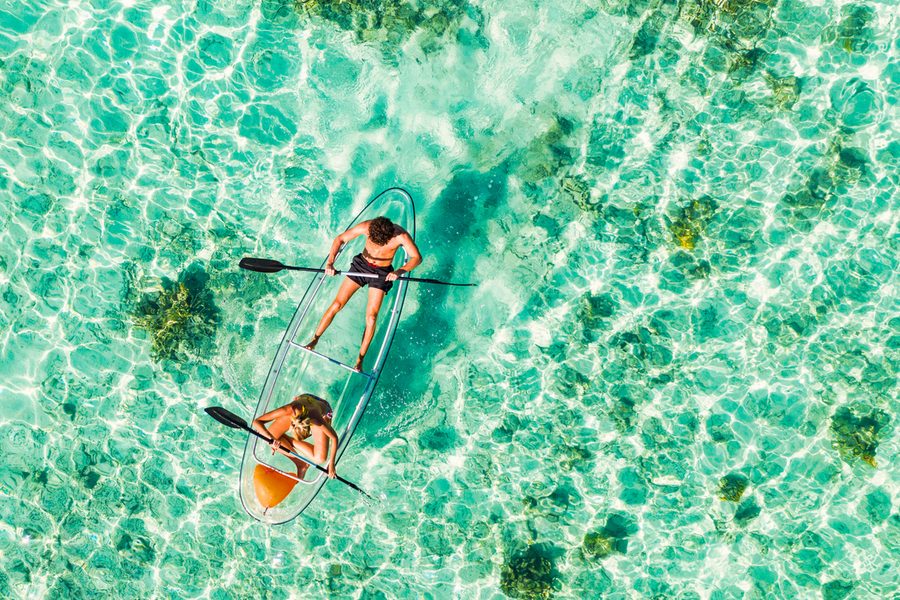 Young couple paddling on glass bottom kayak in tropical ocean